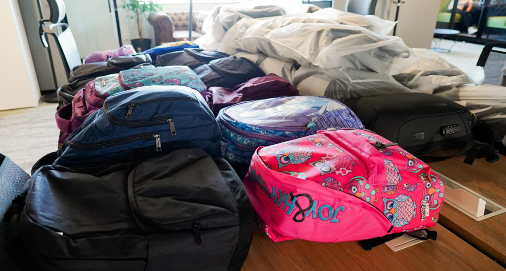 Rows of filled backpacks in various colors and patterns, ready for distribution as part of a corporate back-to-school donation initiative.